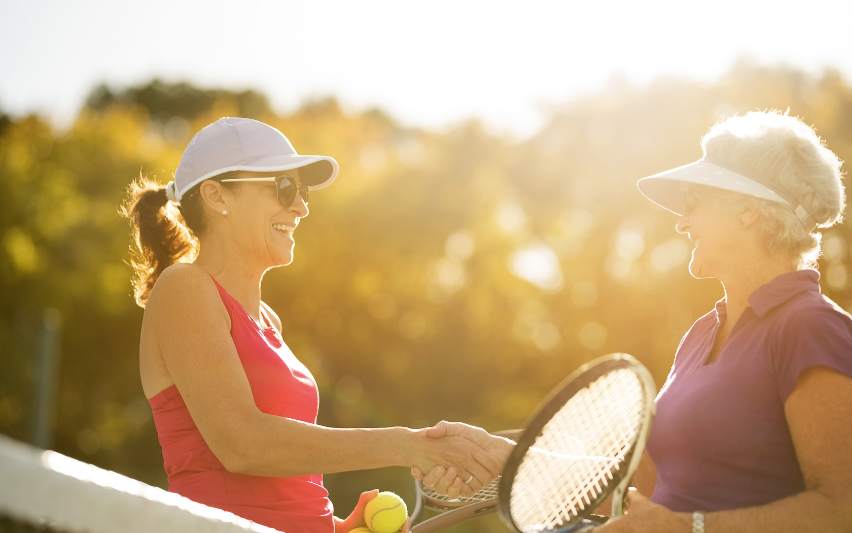 Senior women shaking hands after a friendly game of tennis on bright sunny day.